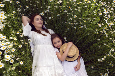 Mother with daughter in a white dress lie on a camomile field