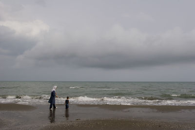 Baby and woman at beach against sky