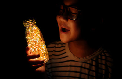 Close-up of woman holding illuminated lighting equipment in darkroom