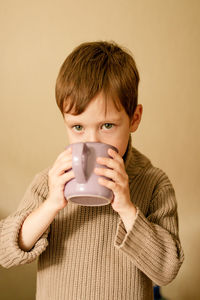 Boy drinks cocoa. warm autumn photography. a boy in a brown sweater drinks from a mug.