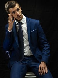 Thoughtful young man sitting on chair against black background