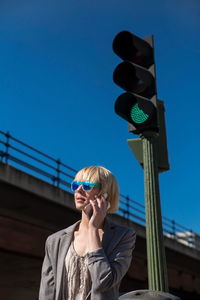 Blonde businesswoman in sunglasses talking on smartphone and looking away at green traffic light on street