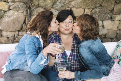 Portrait of woman with raised eyebrows been kissed by female friends during party in yard