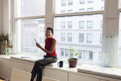 Full length of man using mobile phone while sitting on window