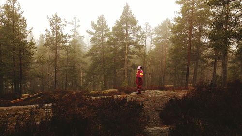 Girl wearing warm clothing standing on field by trees