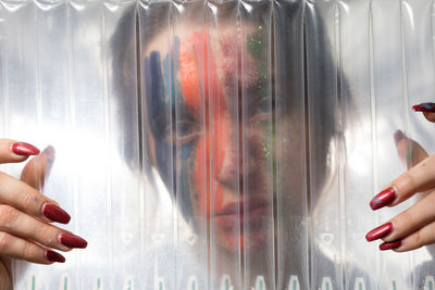 Close-up portrait of woman with painted face seen through plastic