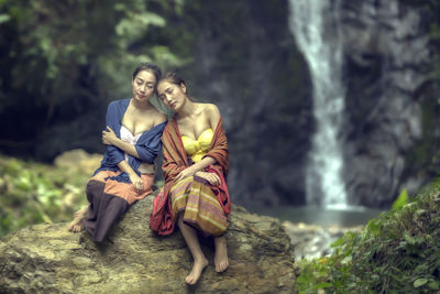 Friends resting on rock against waterfall in forest