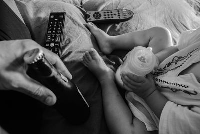 Cropped hand of man holding drink bottle by child with milk bottle on bed