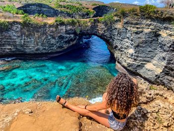 High angle view of woman sitting on cliff by sea