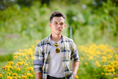 Portrait of young man standing against yellow flowering plants