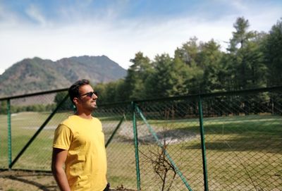 Young man standing by trees against sky