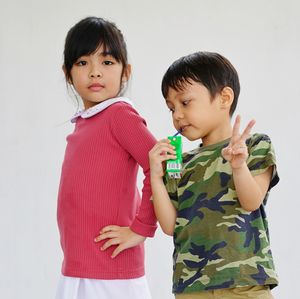 Portrait of cute girl standing with boy gesturing against white background