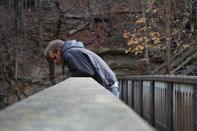 Side view of young man standing by retaining wall in forest