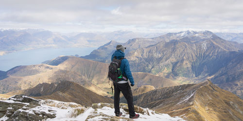 Male hiker standing on top of the mountain enjoying views on beautiful alpine landscape with lake