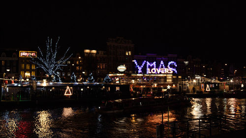 Illuminated buildings by river against clear sky at night