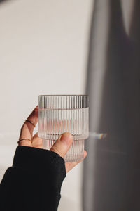 Woman's hand holds a glass of clean water over the white wall in natural sunlight