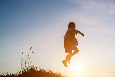 Silhouette woman jumping on field against sky during sunset