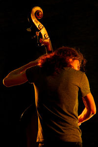 Rear view of man playing guitar while sitting against black background