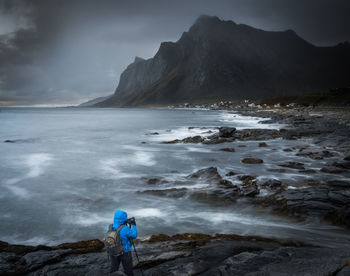 Rear view of woman standing on shore against mountain