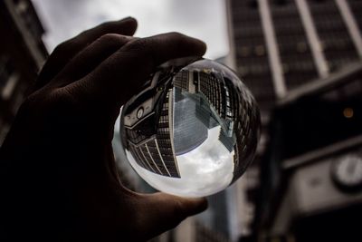 Cropped image person hand holding crystal ball against buildings in city