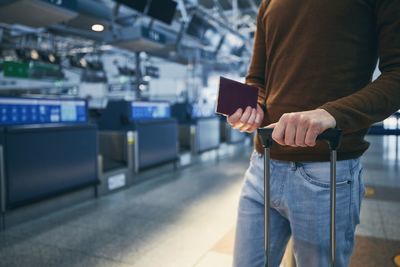 Passenger against check-in counter at airport. hands of young man holding suitcase and passport.