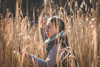 Side view of woman holding navigational compass while standing amidst plants