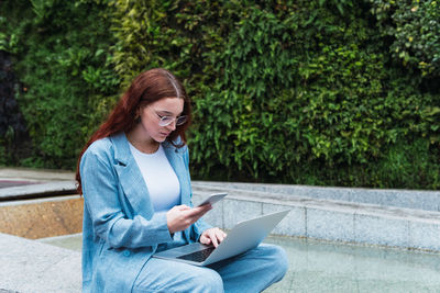 Redhead woman reading text business message from her managers connected to public internet outdoors