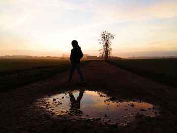 Boy standing on field against sky during sunset