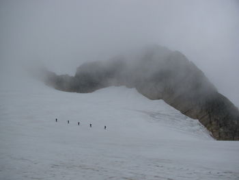 Distant view of silhouette people hiking on snow covered field in foggy weather