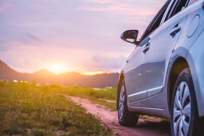 Car on road amidst field against sky during sunset