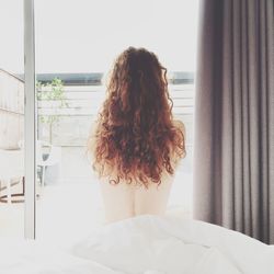 Rear view of topless woman sitting on bed at home