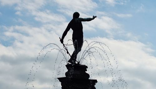 Low angle view of man standing by sculpture against sky