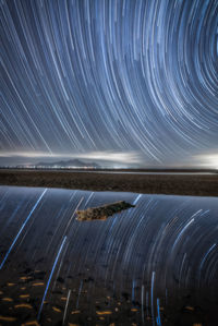 Light trails in sea against clear sky at night