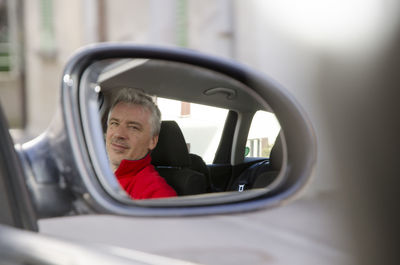 Portrait of man reflecting on side-view mirror of car