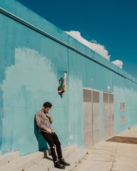 Full length of man sitting against wall against building