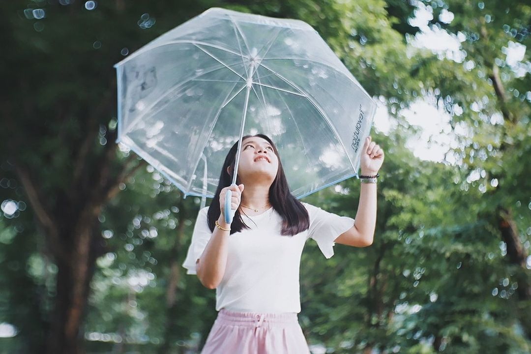 one person, real people, umbrella, women, front view, leisure activity, standing, holding, tree, waist up, focus on foreground, nature, lifestyles, protection, young women, young adult, rain, casual clothing, wet, outdoors, human arm, arms raised, innocence