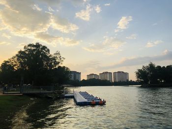 Boat in river by buildings against sky during sunset