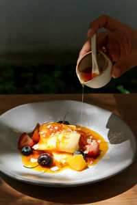 Cropped hand pouring sauce in dessert on table