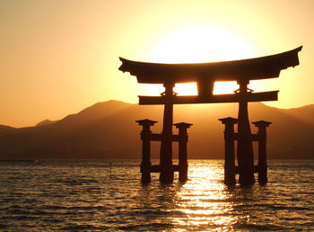 Silhouette torii gate amidst river against sky during sunset
