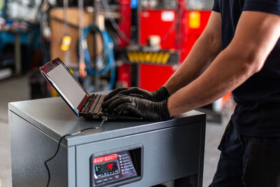 Adult man in using laptop to program broken machine during work in modern workshop