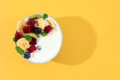 Yoghurt bowl with fresh fruit topping and mint leaves on yellow background. summer healthy concept 