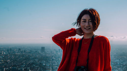 Portrait of smiling young woman standing against cityscape