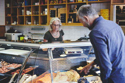 Customer showing seafood at retail display to saleswoman in deli