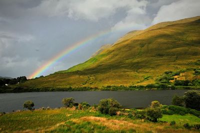 Scenic view of river against rainbow over green mountains