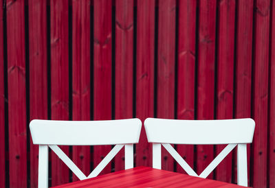 Close-up of chairs and table against red wooden wall