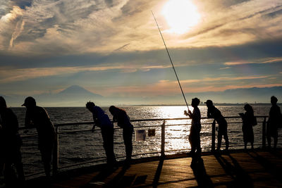 Silhouette people fishing on promenade against sky during sunset