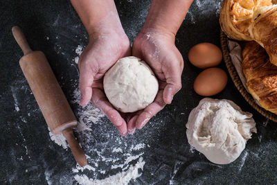 High angle view of cropped hands holding dough over table