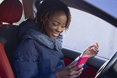Smiling young woman using mobile phone while sitting in car