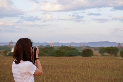 Rear view of woman photographing farm against sky