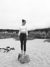 Full length of girl standing on tree stump at beach against sky